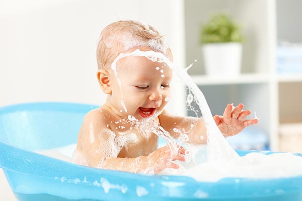 A baby boy enjoying a bath in a small blue tub.