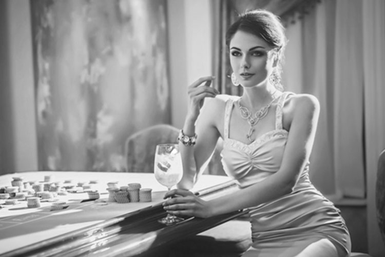 A woman in a svelte dress sitting next to a poker table drinking a martini