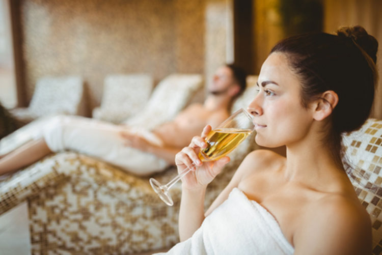 Woman drinking champagne in a bathrobe with her husband relaxing in the background