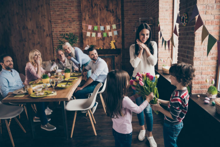 Woman being surprised by kids holding flowers while the family looks on